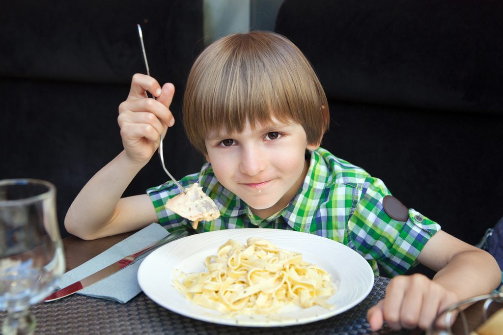 Happy boy eating a plate of pasta with salmon
