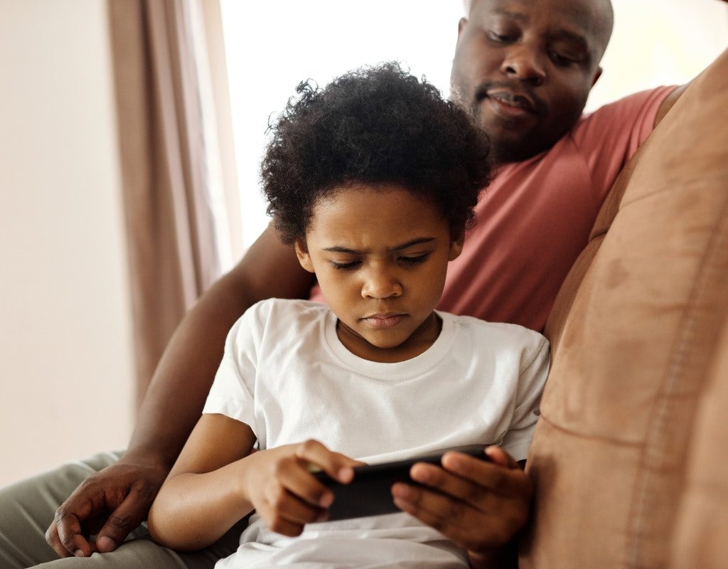 A father watching his son play a game on a phone