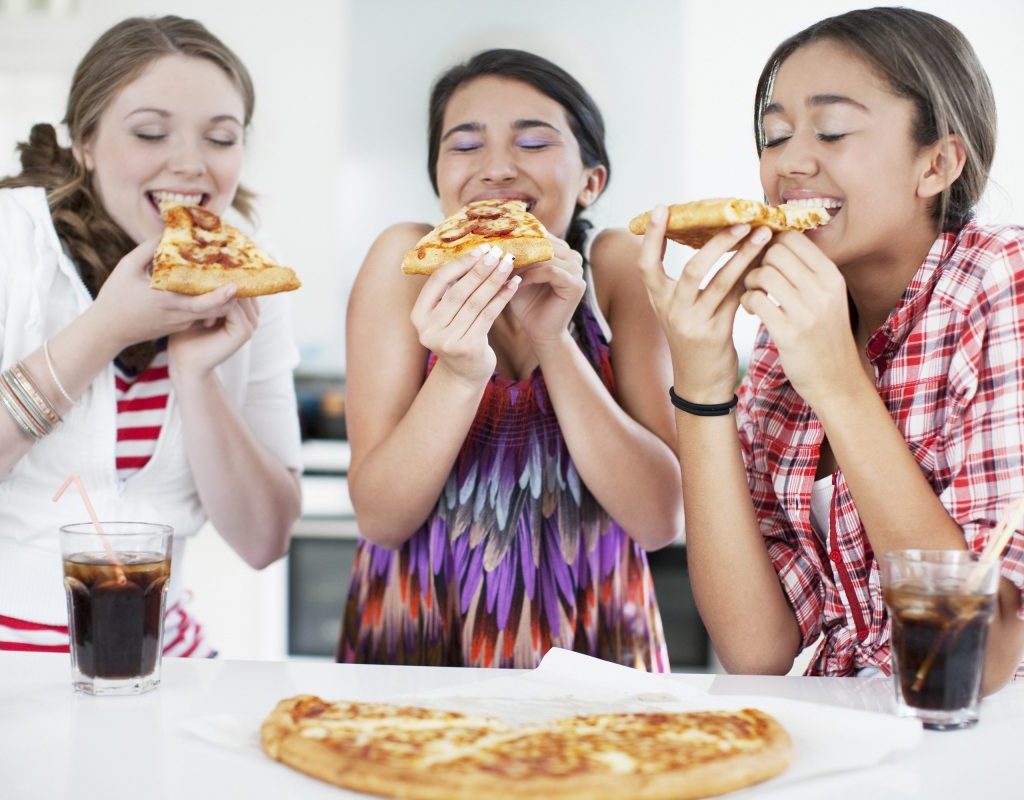Teenage girls eating pizza happily together.