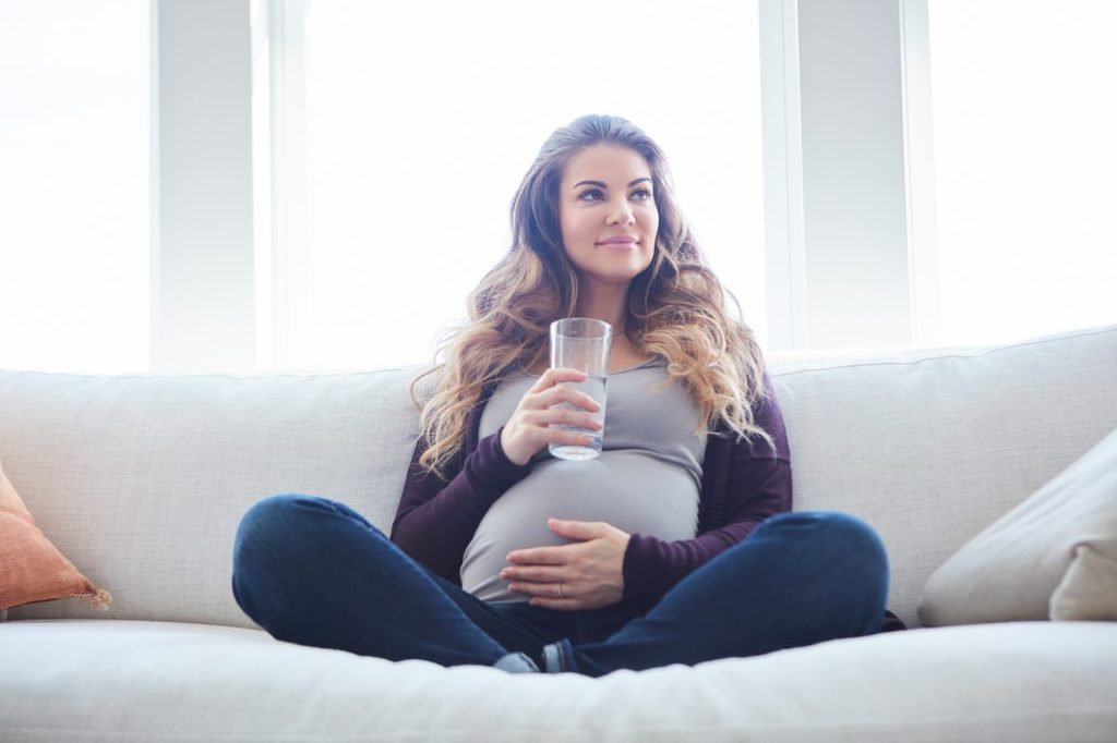 Pregnant woman drinking water while on the couch.