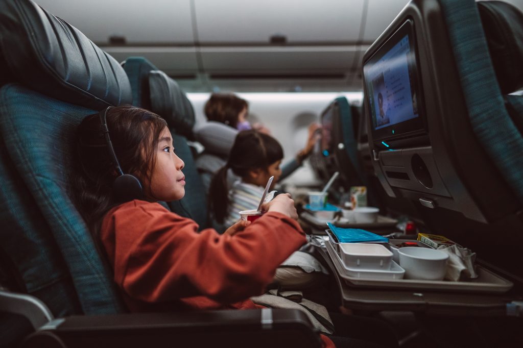 Little girl watching movie on the seat-back TV screen while enjoying her airline meal