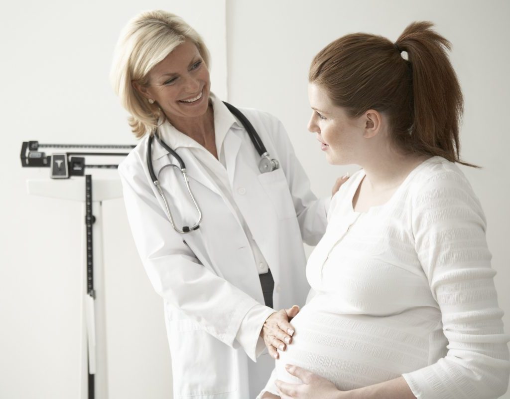 Female doctor touching pregnant woman's stomach, smiling