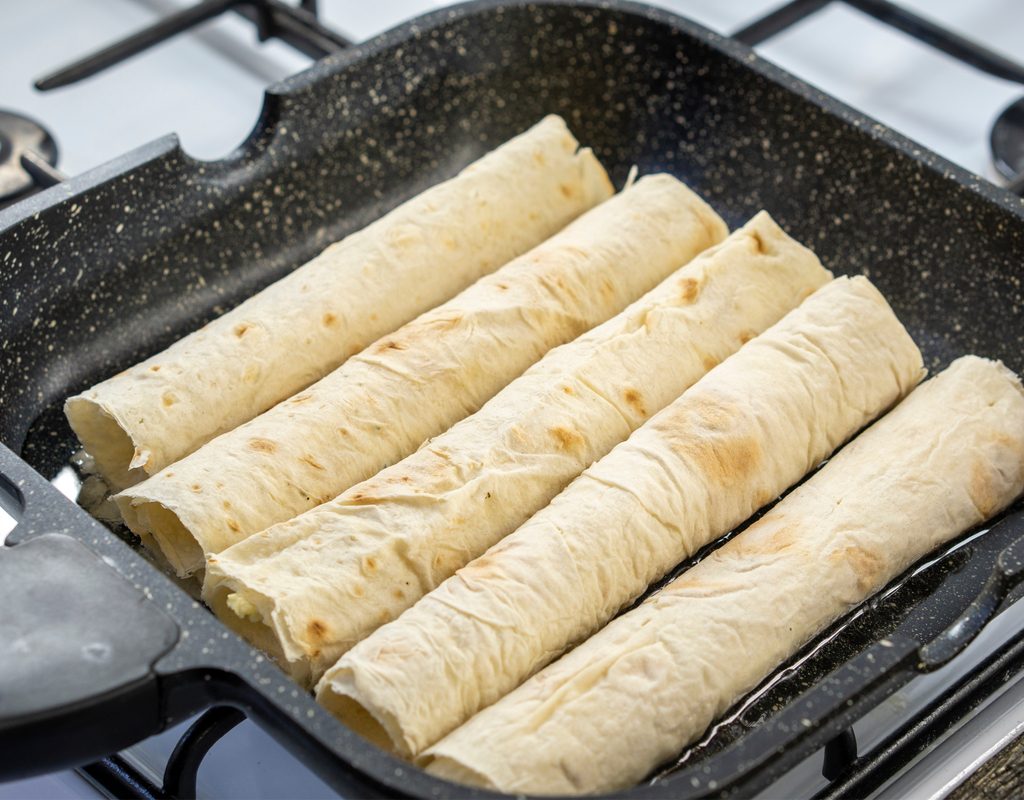 batch of taquitos cooking in a pan on the stove