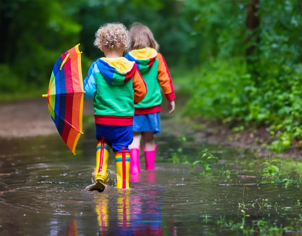 two toddlers walking through a large puddle in their rain boots