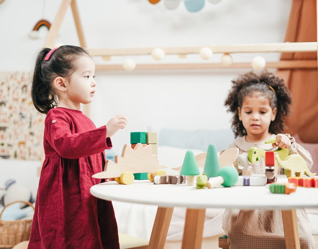 Two toddlers playing with toys on a table.