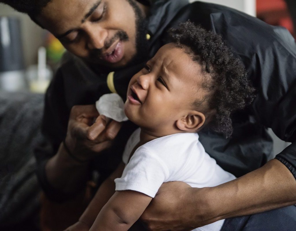 A father wiping a fussy baby's nose.