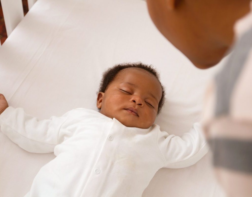 A parent looking over their baby sleeping in their crib.