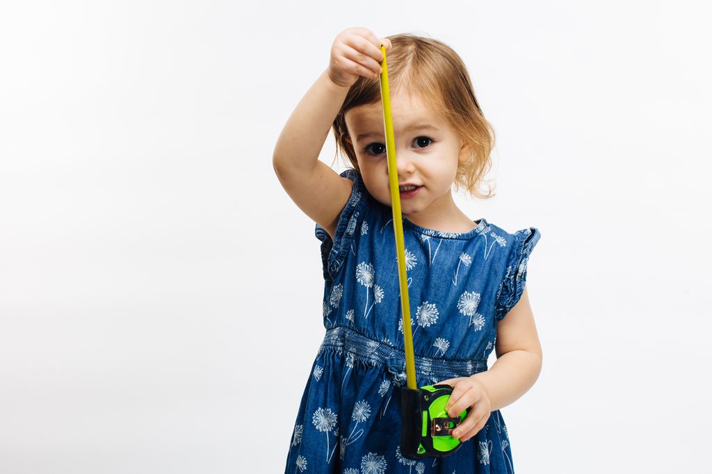 A toddler girl holding a measuring tape apart.