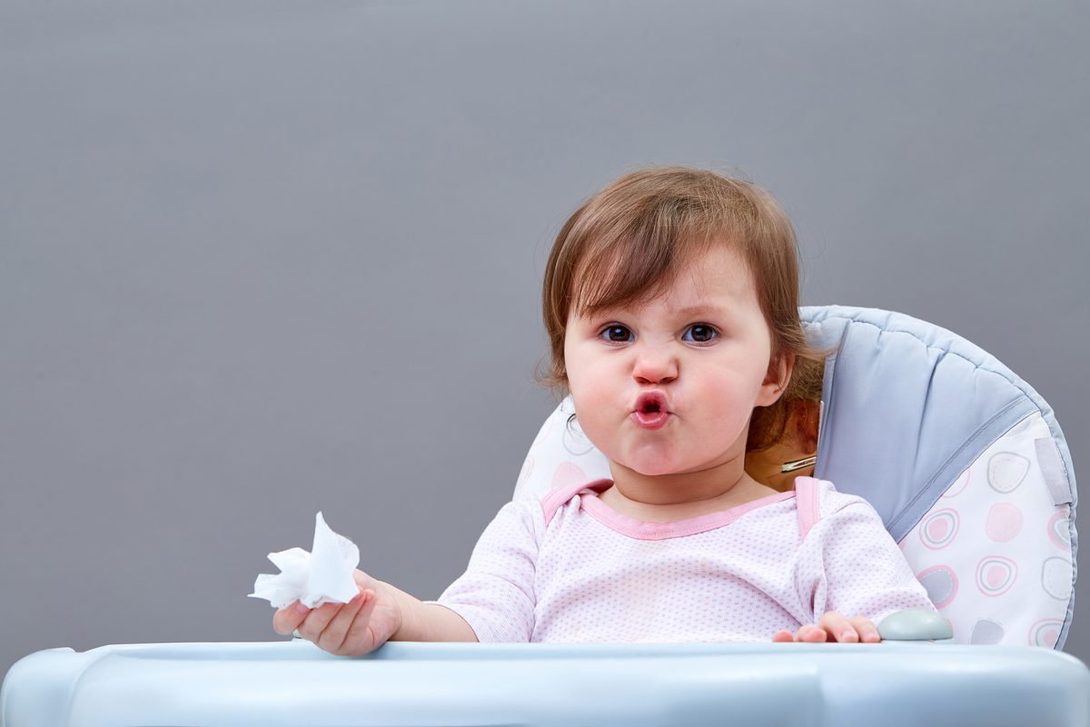 A little child holding a tissue in their hand and crinkling their face up.