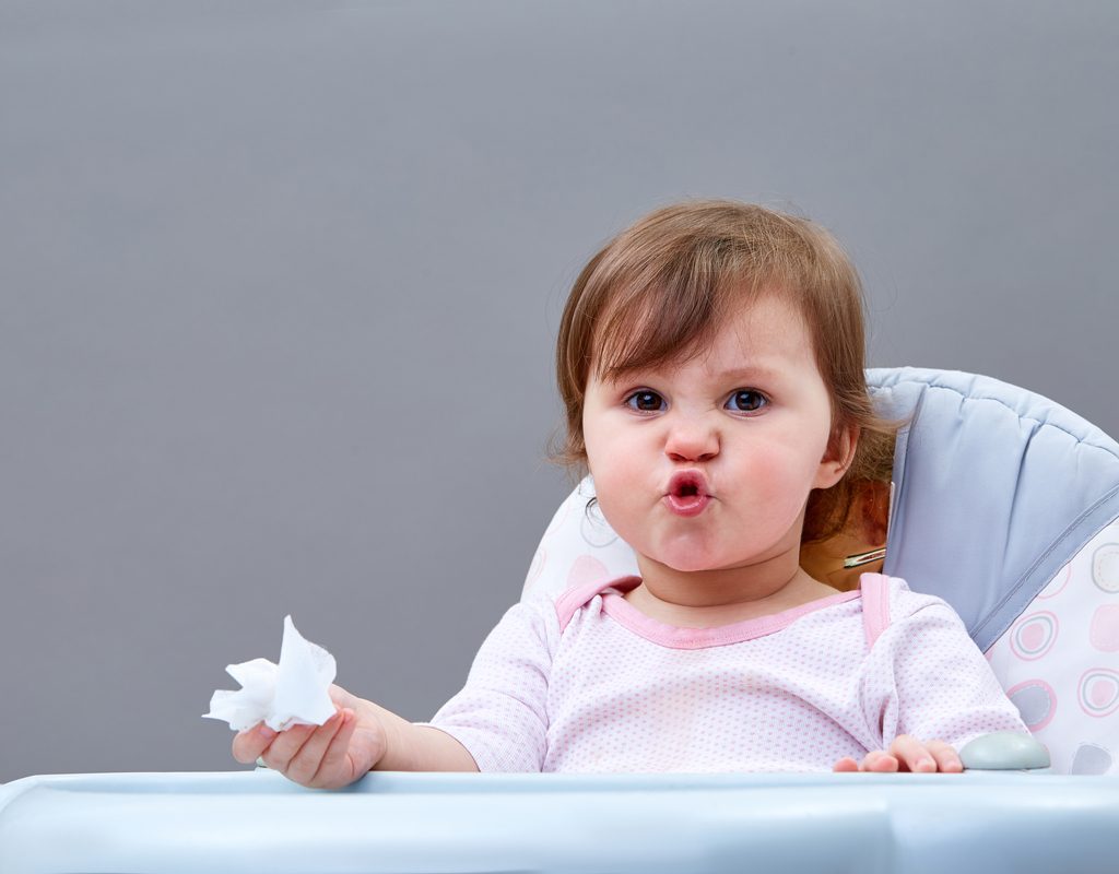 A little child holding a tissue in their hand and crinkling their face up.
