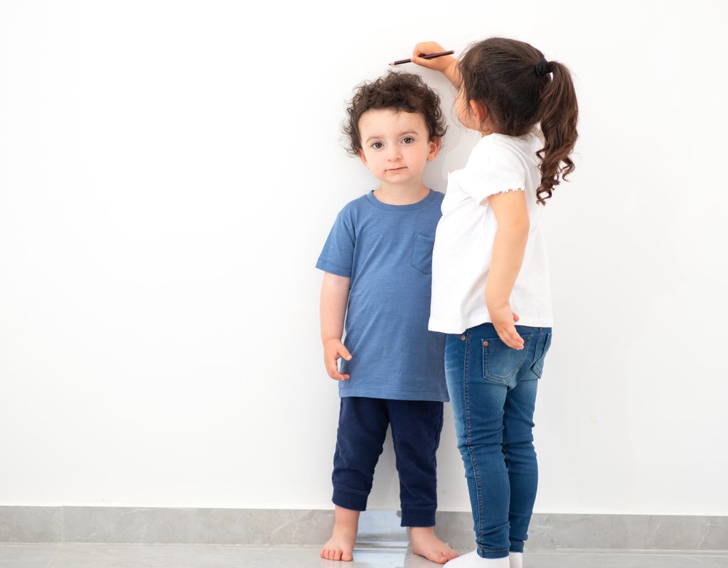 One young child measuring the height of another little child.