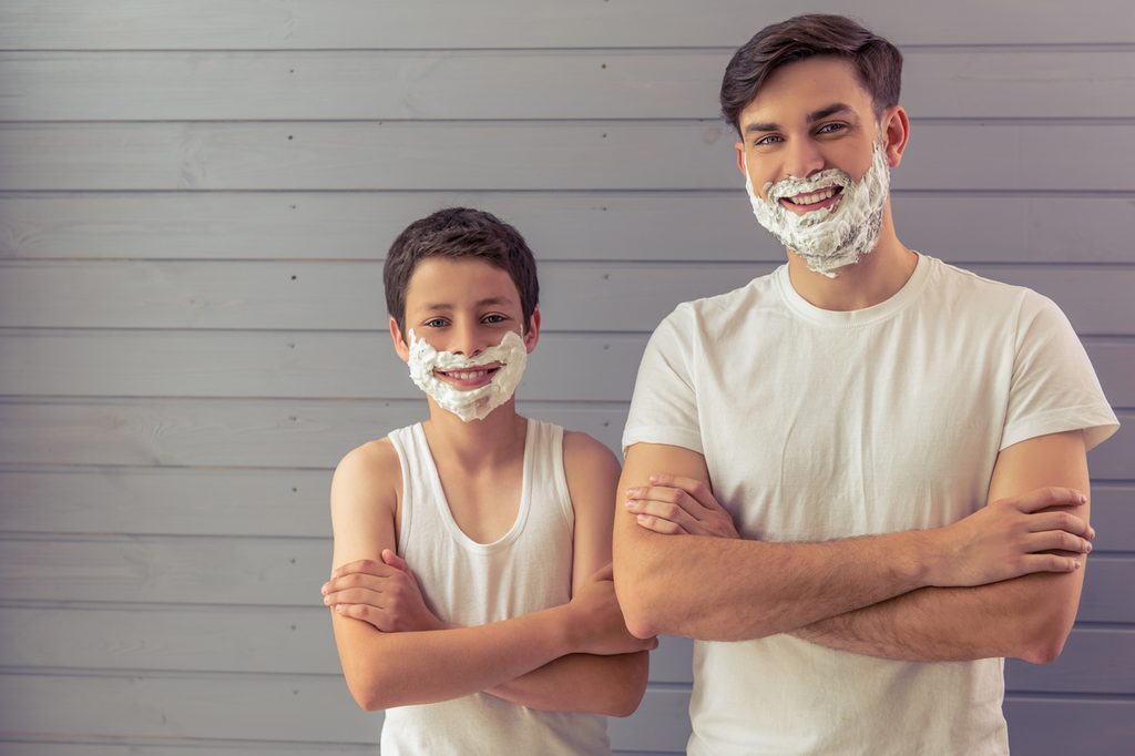 A father and son with shaving cream on their faces getting ready to shave.
