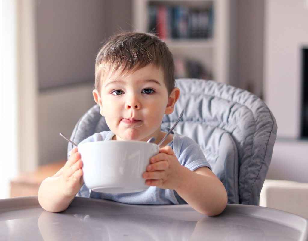 A young toddler holding up a bow for more food.