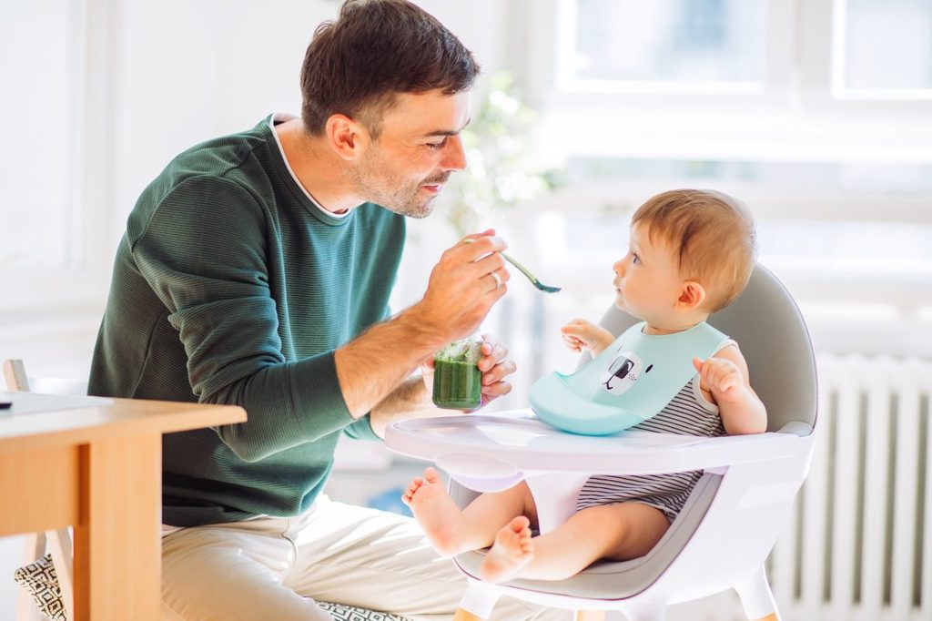 A parent feeding their baby food while the baby wears a bib.