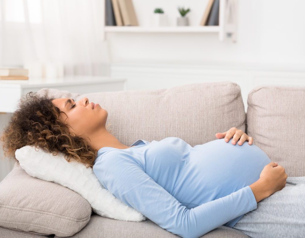 A pregnant woman lying on the couch holding her stomach