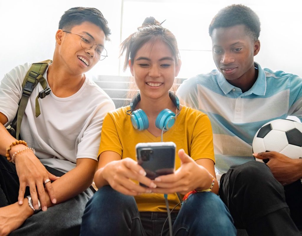 A group of teens looking at a cellphone.