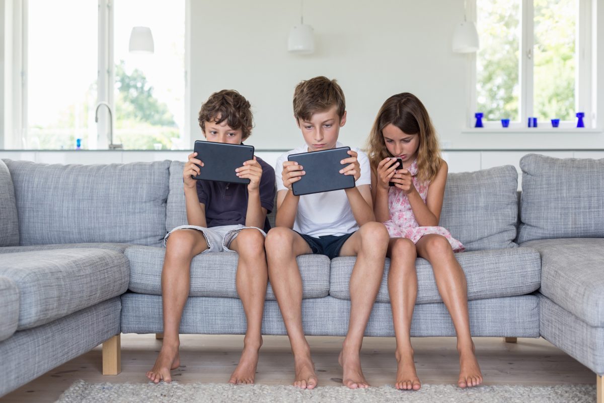 Three kids sitting on the couch on their devices playing a game.