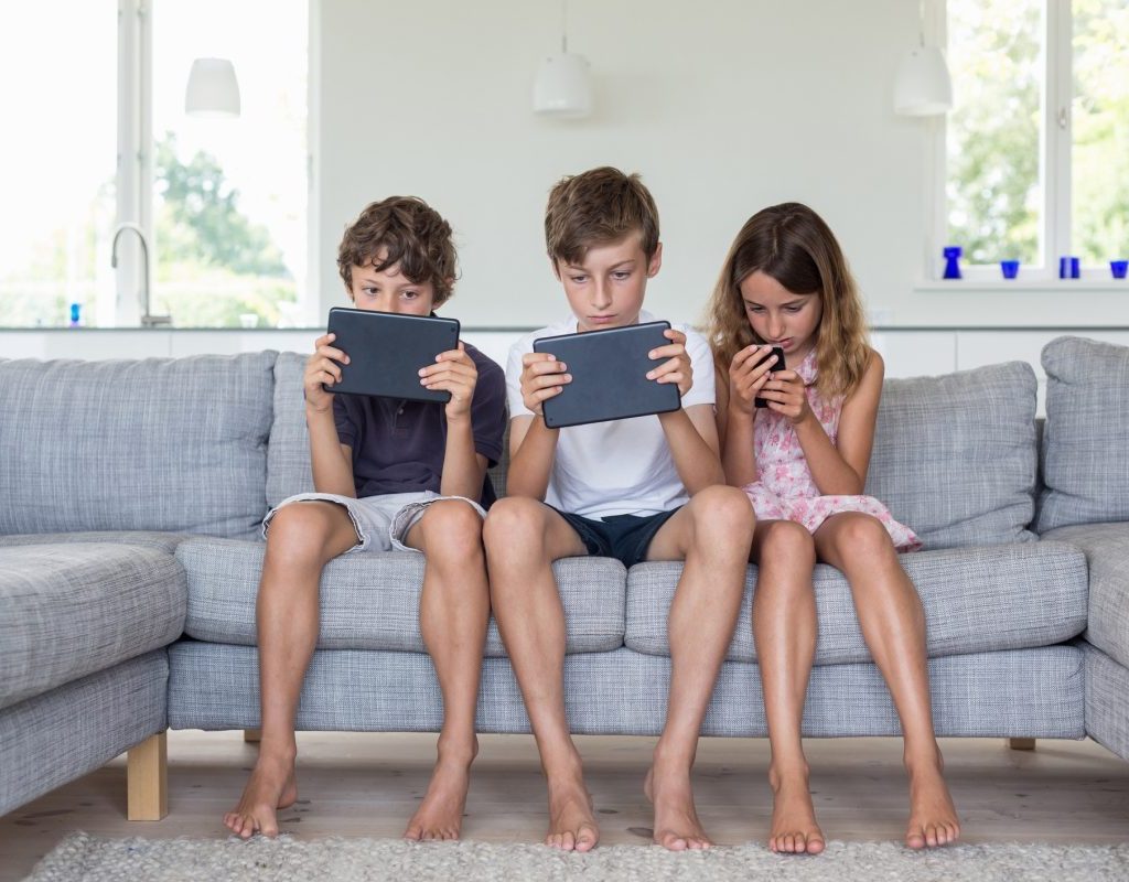 Three kids sitting on the couch on their devices playing a game.