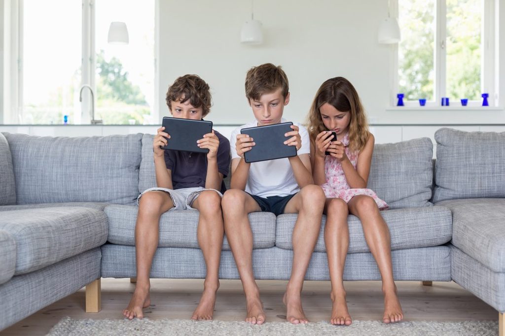 Three kids sitting on the couch on their devices playing a game.