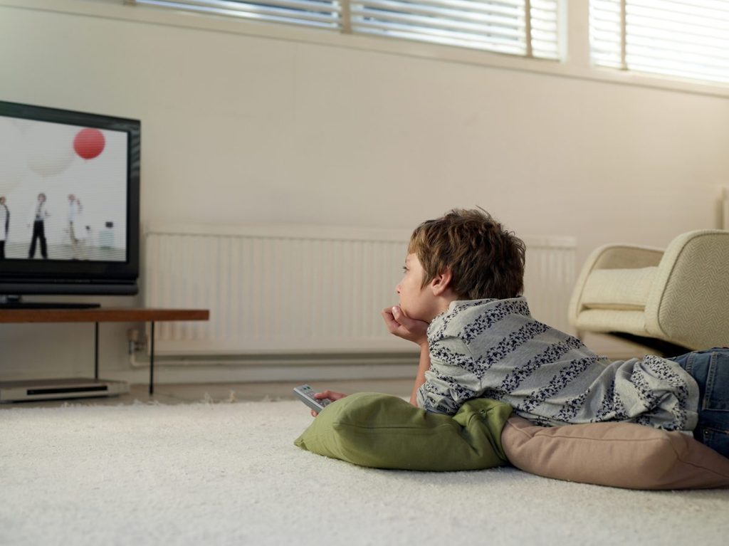 A child watching tv while lying on the floor.