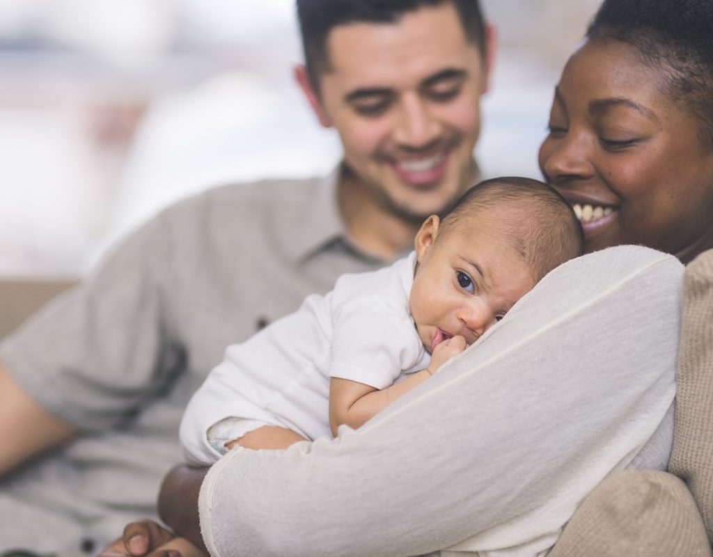 A mother holding her newborn baby with her partner looking on