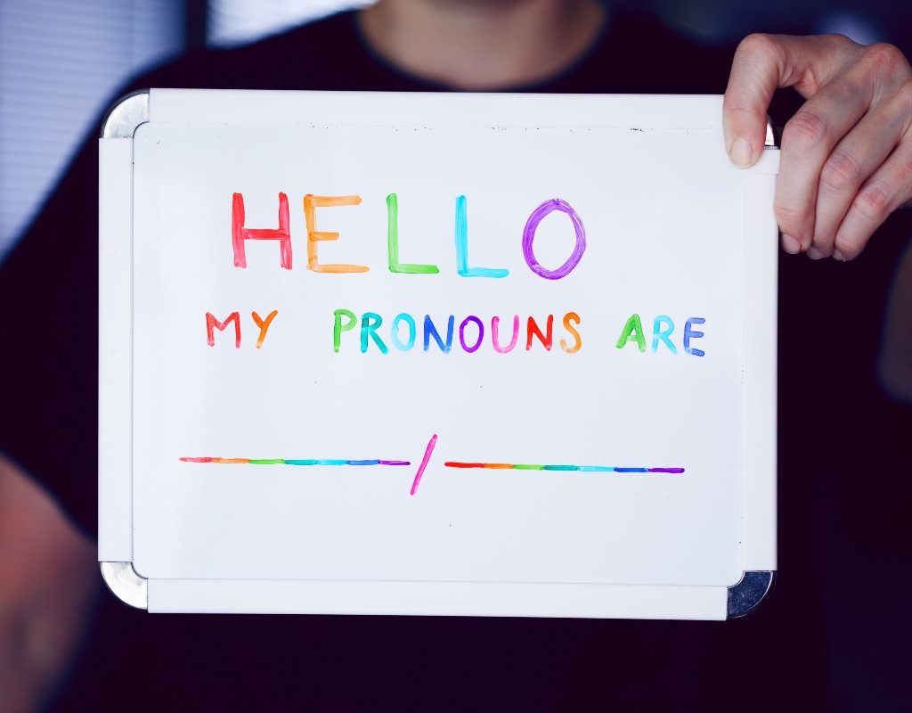 A child holding up a whiteboard that says, "Hello, my pronouns are"