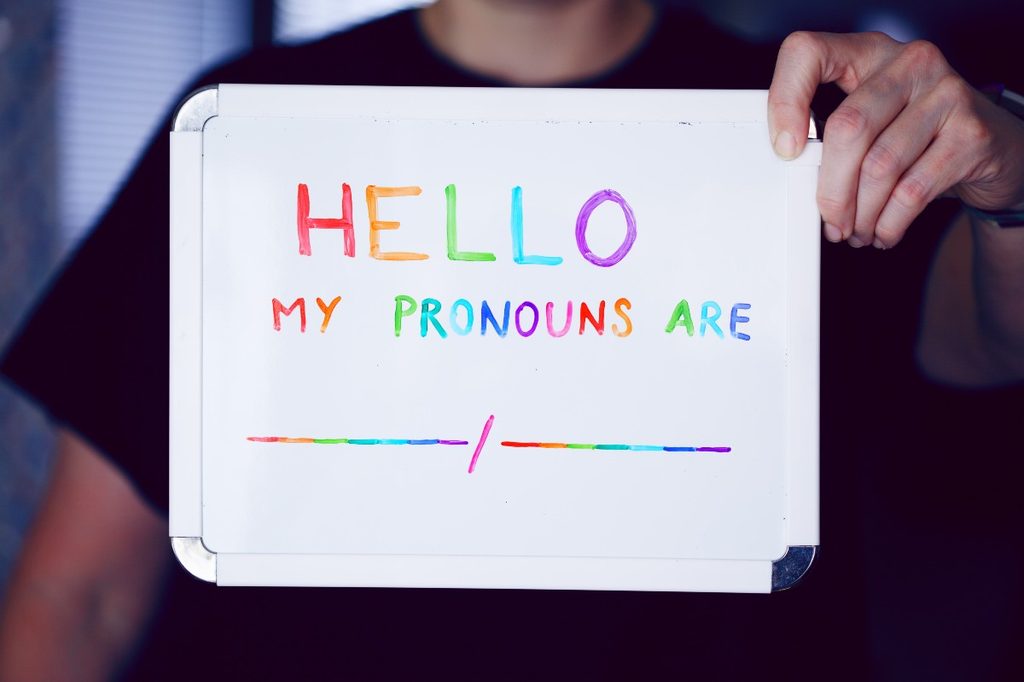 A child holding up a whiteboard that says, "Hello, my pronouns are"