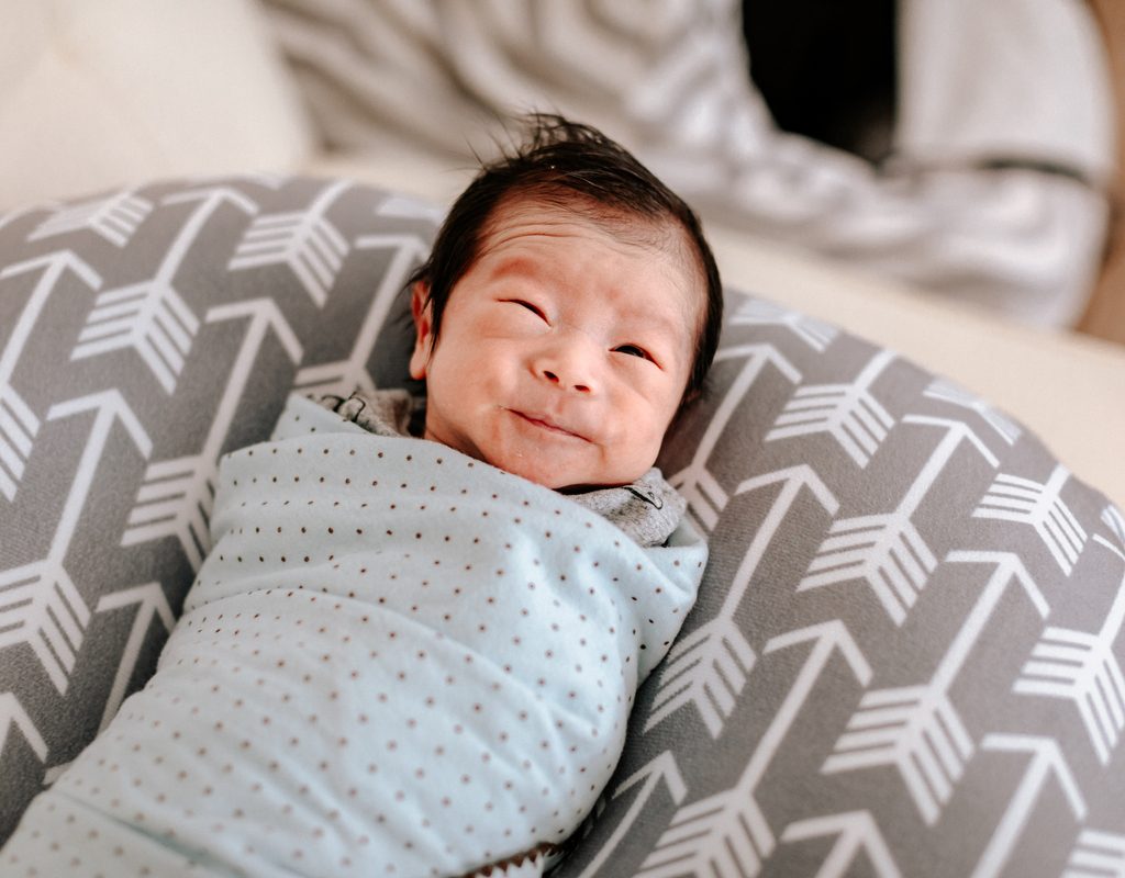 A swaddled baby supported by a pillow.