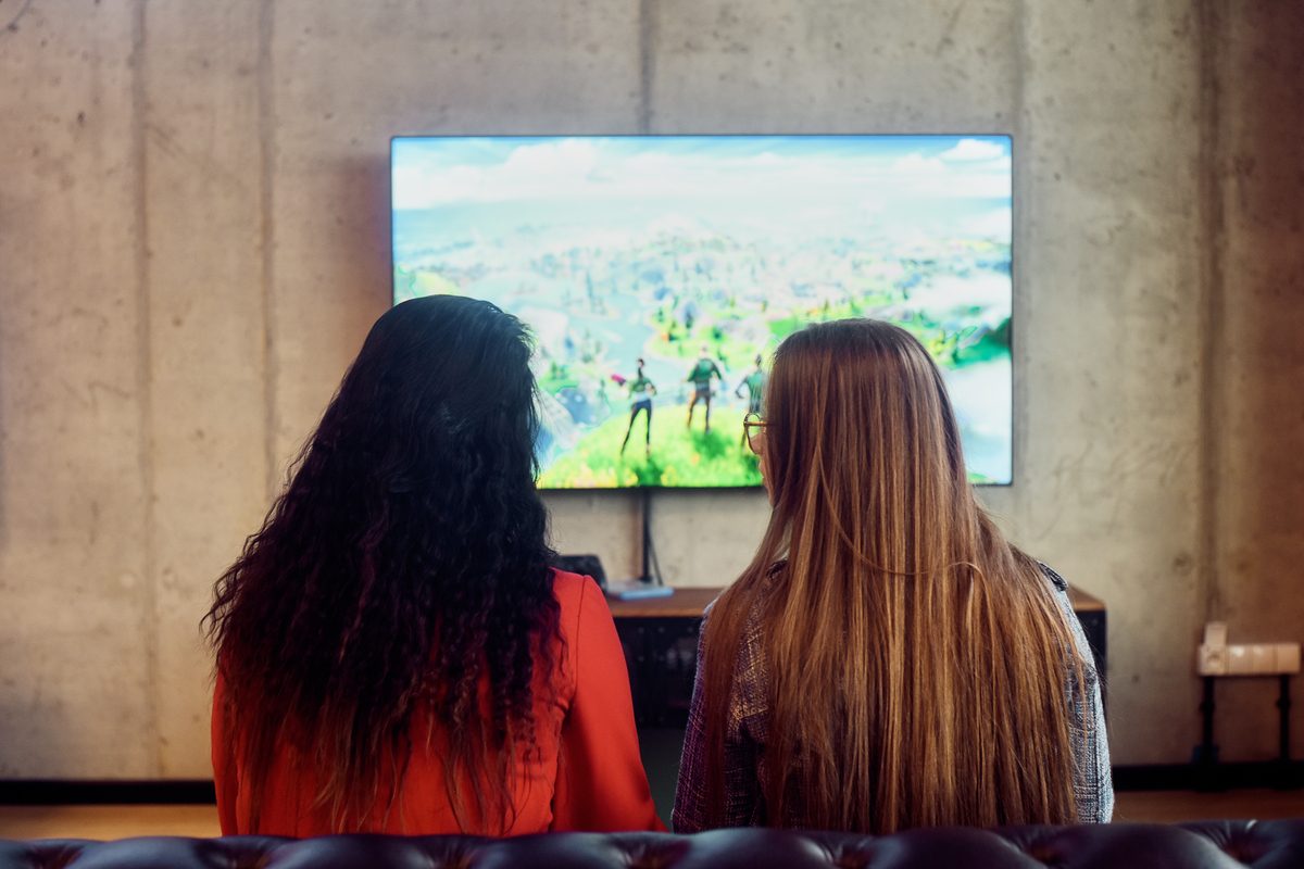 Two girls sitting next to each other playing Fortnite.