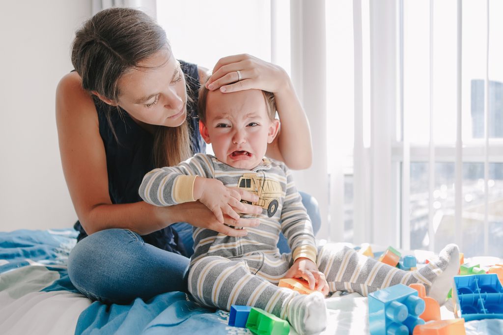 A mother holding her crying toddler sitting on the bed