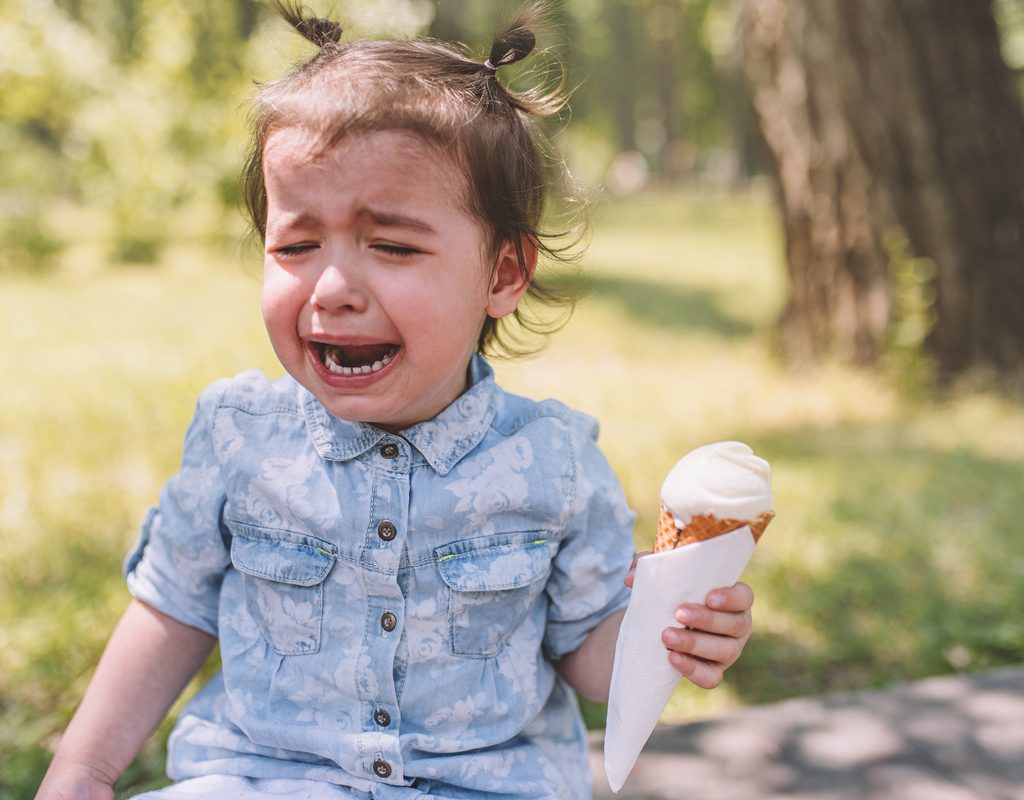 A crying toddler holding an ice cream con.e