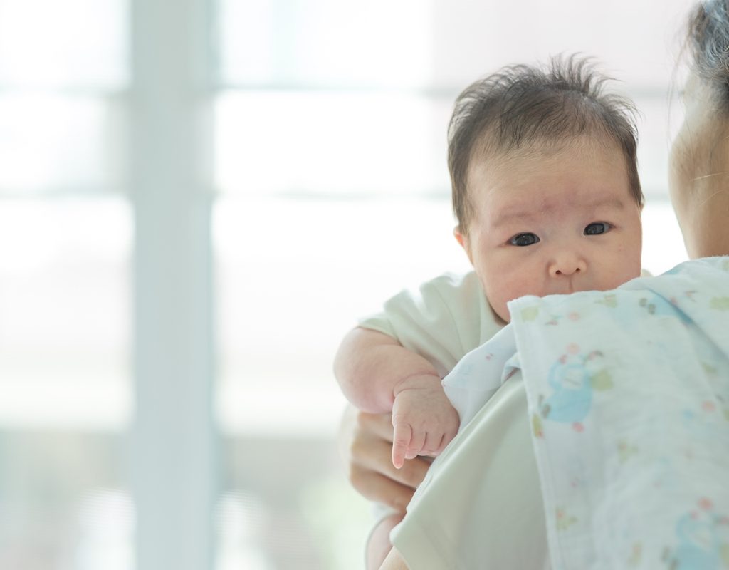 A parent holding a little baby over their shoulder.