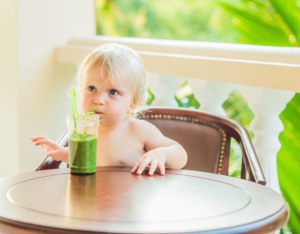 A baby drinking a green drink.