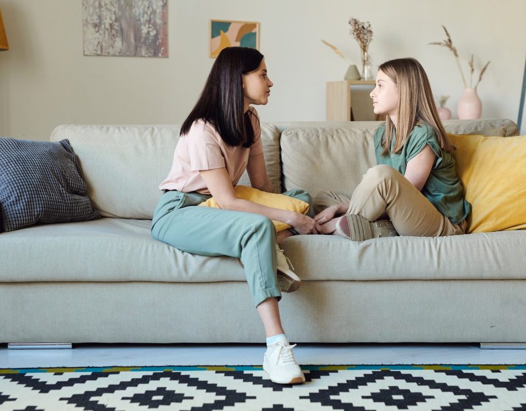 A mother and daughter having a conversation while sitting on the couch together.