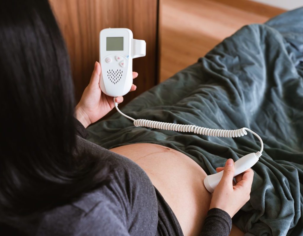 A pregnant woman using a monitor on her belly at home.
