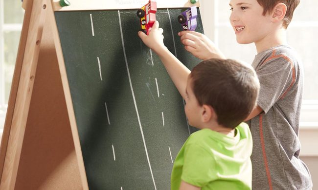 Two boys playing with the Melissa & Doug Deluxe Wooden Standing Art Easel.