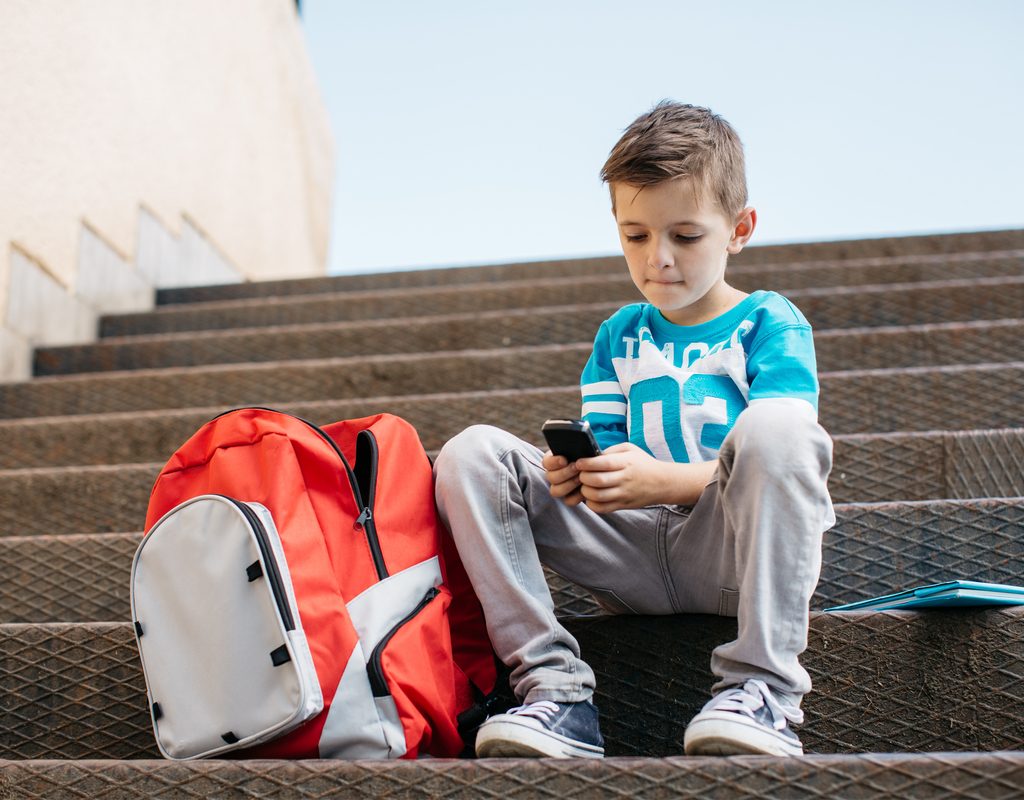 Boy texting mom after school on his cellphone.