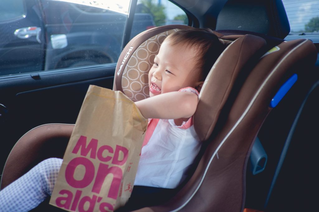 A toddler reaching into a bag of fast food in the car