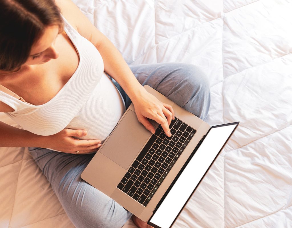 A pregnant woman holding a laptop in her lap while holding her belly