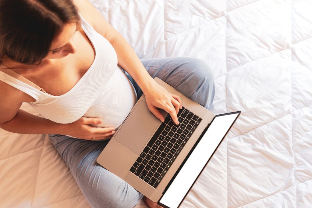 A pregnant woman holding a laptop in her lap while holding her belly.