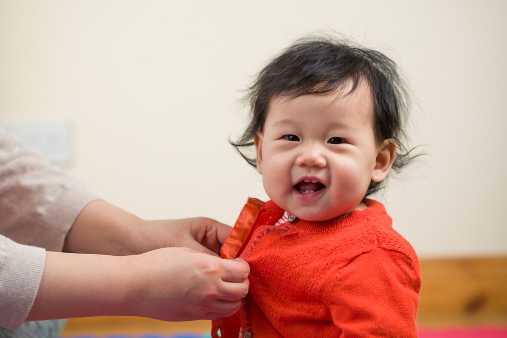 A little baby girl getting a sweater buttoned on them.