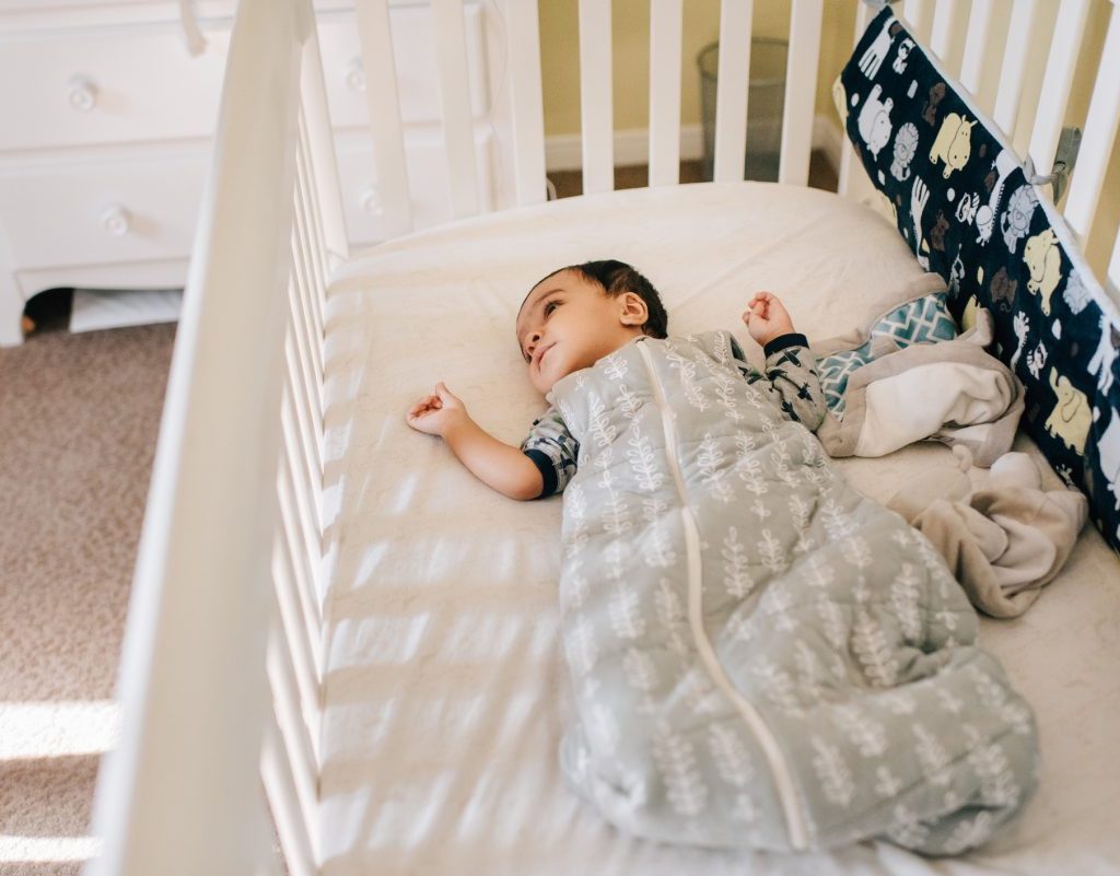 A baby awake in their crib in a sleep sack