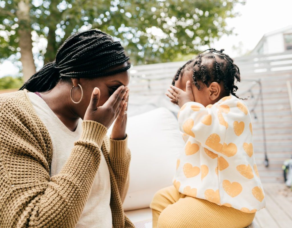 A mother and young child playing peekaboo outside.