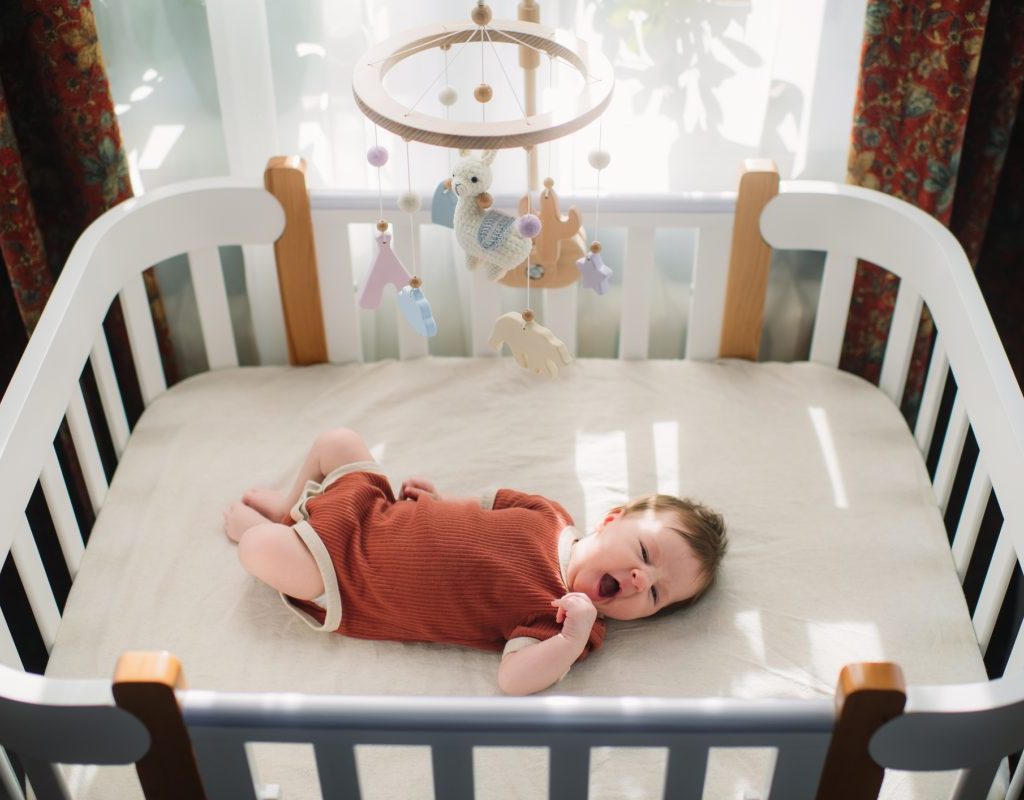 A baby in crib wearing a onesie looking at the mobile