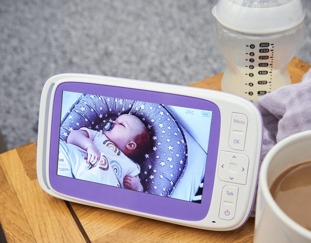 A baby monitor video sitting on a side table by a bottle and cup of coffee