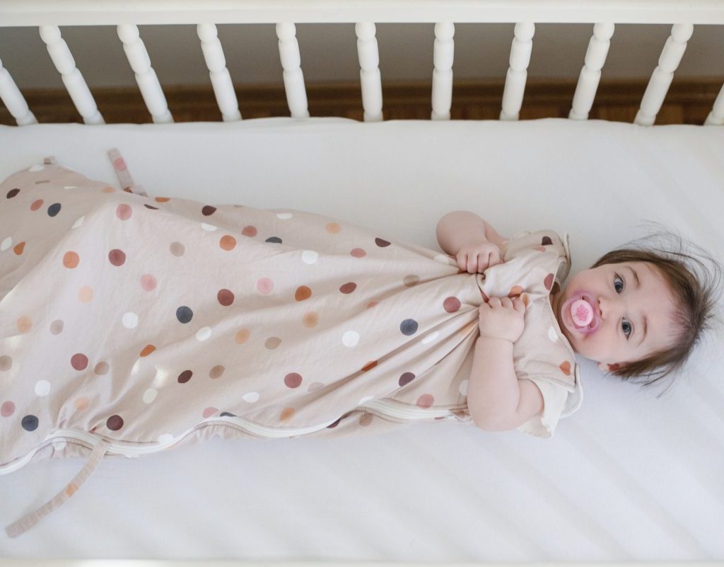 A baby in a sleep sack in their crib