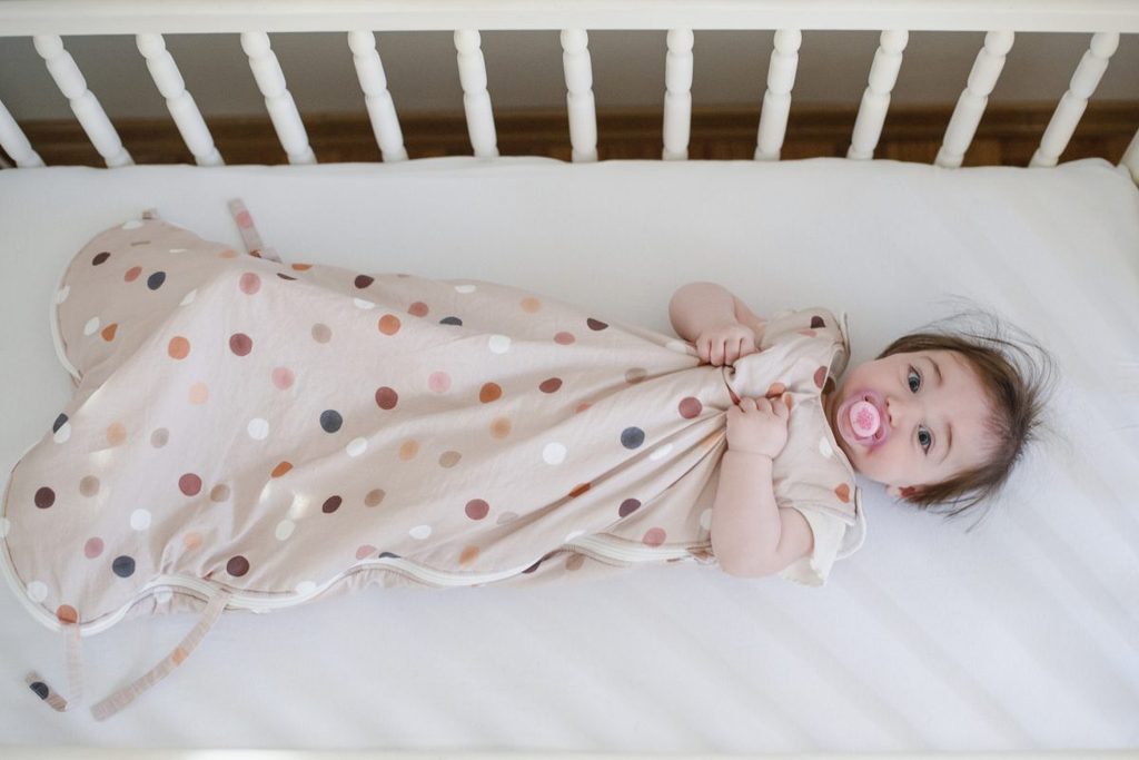 A baby in a sleep sack in their crib.