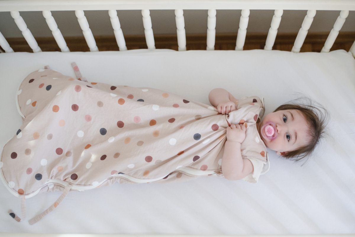 A baby in a sleep sack in their crib.