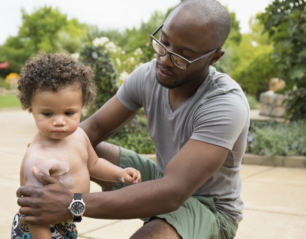 A father putting sunscreen on the body of his young child.