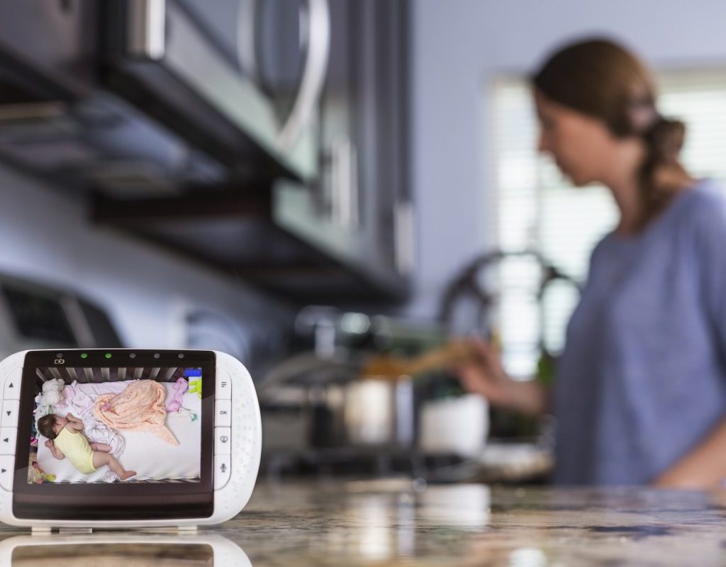 A woman cooking in the background with a baby monitor video in the forefront